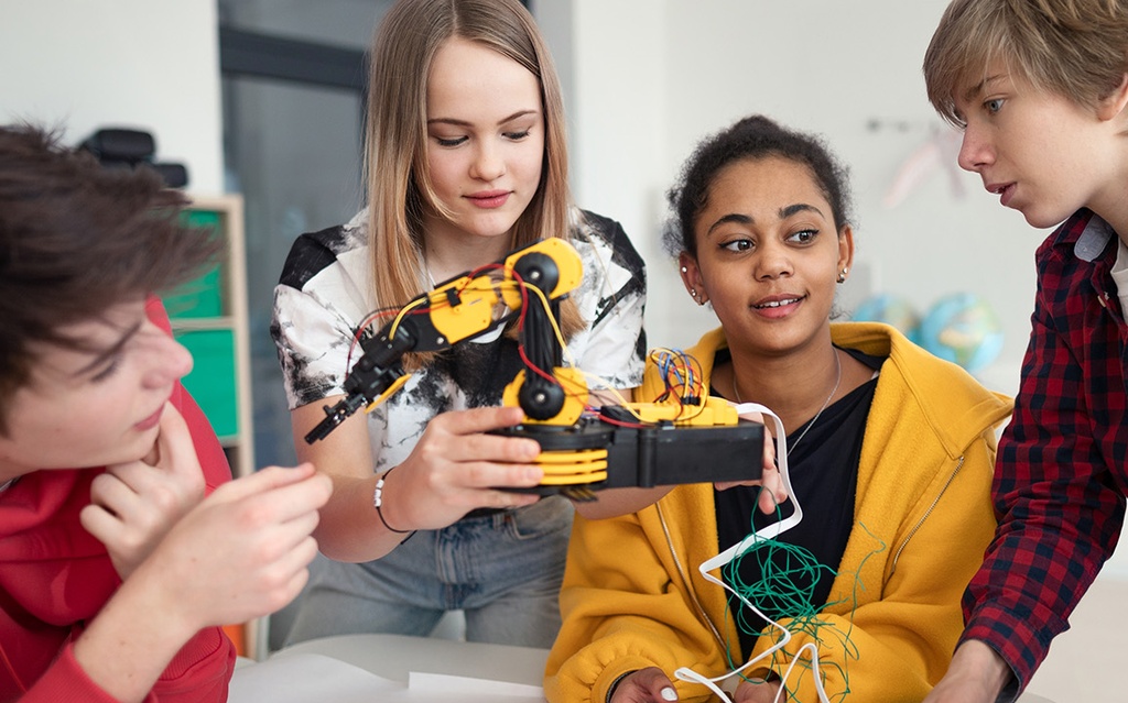 Fünf Jugendliche tüfteln gemeinsam an einem Roboterarm.